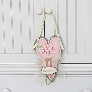 May include: A pink felt heart with a green felt trim and a pink fabric rose. The heart has a white ribbon with a beaded trim and a tag that says "Best Friends".