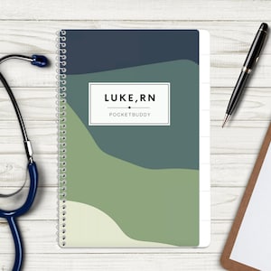May include: A spiral-bound notebook featuring a cover with abstract wavy layers in shades of dark blue, teal, and light green. A white rectangular label in the center displays the black text LUKE, RN and POCKETBUDDY. A stethoscope and pen are nearby.