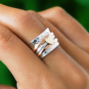 May include: A silver ring with a hammered texture, rose gold band, and a small gold heart. The ring has a unique design with multiple bands that spin freely. The ring is a piece of jewelry.