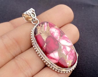 May include: Oval pendant with a composite stone in red, pink, white, and gold hues. The stone is set in a silver-coloured metal with a decorative border and bail.