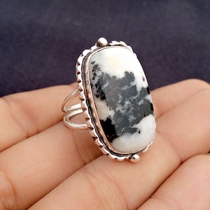 May include: A silver ring featuring a large, rectangular stone with a striking black and white pattern. The stone is set in a decorative bezel with a scalloped edge. The ring has a double-band design.