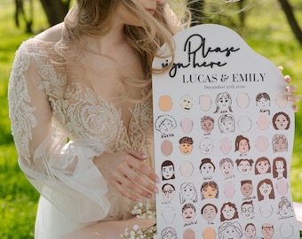 Può includere: Un cartello in legno bianco con il testo "Please sign here" in corsivo nero. Il cartello include anche i nomi "Lucas & Emily" e la data "December 21th 2026". Il cartello ha uno sfondo bianco con un bordo rosa e presenta una griglia di 36 facce di cartoni animati per gli ospiti da firmare.