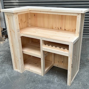 May include: A wooden bar counter with a built-in shelf and wine rack. The counter is made of unfinished pine wood and has a natural wood finish.