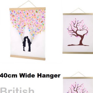 May include: A set of two 40cm wide wooden picture hangers with a black string. The hangers are shown with two different prints, one with a couple kissing under a sky full of colourful balloons and the other with a pink tree with a heart-shaped opening in the branches.