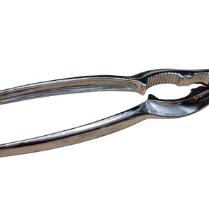 May include: A silver nutcracker with a textured handle and a serrated jaw. The nutcracker is designed to crack nuts.