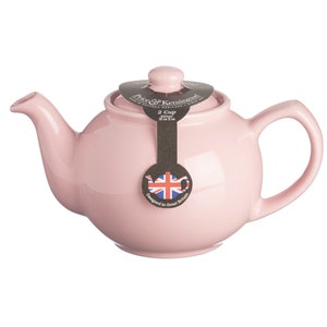K&ouml;nnte beinhalten: Hellrosa Keramik-Teekanne mit rundem Korpus, gebogenem Griff und Ausguss. Der Deckel hat einen kleinen Knopf. Ein schwarzes Etikett zeigt "2 Cup" und "Designed in Great Britain."