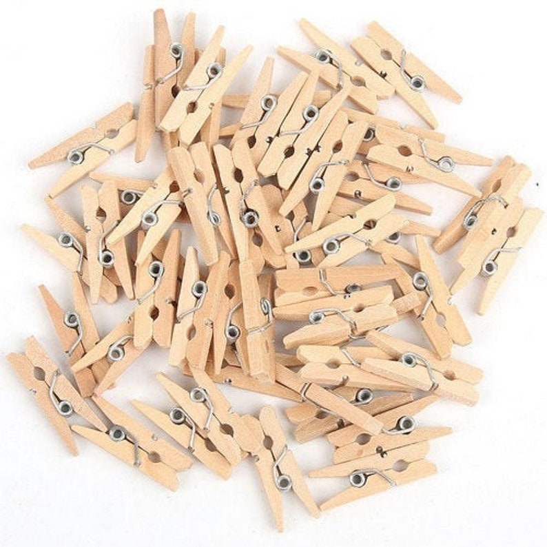 May include: A pile of natural wood clothespins with silver metal springs. The clothespins are approximately 2 inches long.