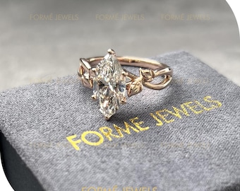 May include: Rose gold engagement ring featuring a marquise-cut diamond. The ring has a floral design with leaf accents on the band. The ring is displayed on a gray velvet surface with the text "FORME JEWELS".