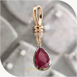 May include: A gold pendant with a teardrop-shaped ruby gemstone. The ruby is framed by a silver-colored metal and hangs from a gold bail. The pendant has a decorative gold section with small, clear stones.