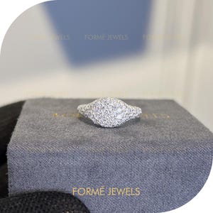 May include: A diamond ring featuring a cluster of small, round diamonds set in a white metal band. The ring is presented on a grey box with the gold text "FORME JEWELS".