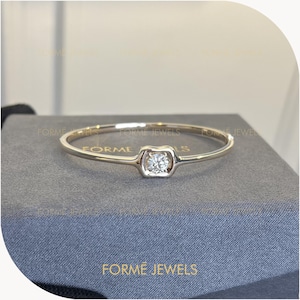 Puede incluir: Una delicada pulsera de oro con un diamante cuadrado en el centro. La pulsera tiene un diseño minimalista con una banda delgada. El nombre de la marca "FORME JEWELS" es visible en la superficie inferior.