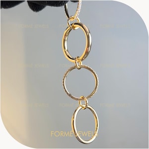 May include: A gold-colored necklace featuring three interconnected circular pendants. The top and bottom circles are plain, while the middle circle is adorned with small, sparkling embellishments. The necklace is suspended from a chain with additional small embellishments.