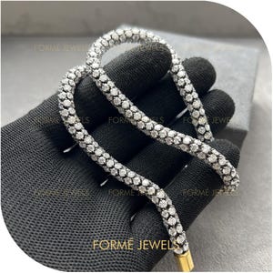 May include: A dazzling necklace with a silver chain adorned with small, round, white gemstones. The necklace is held by a gloved hand. The clasp is gold. The brand name "FORME JEWELS" is visible.