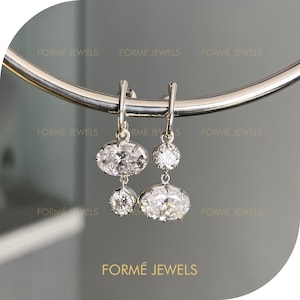 May include: A pair of silver drop earrings with oval and round clear gemstones. The earrings are suspended from a silver hoop. The brand name "FORME JEWELS" is displayed at the bottom of the image.