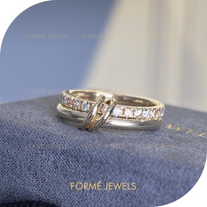 May include: Three gold rings stacked together. The top ring features small, clear and pink gemstones. The middle ring is plain gold, and the bottom ring is silver. The rings are intertwined. The brand name "FORME JEWELS" is visible.