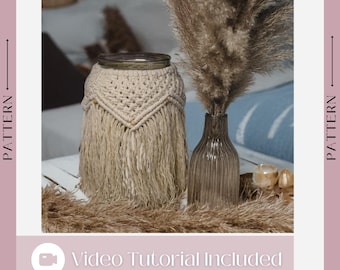 Peut inclure: Un vase en macramé beige avec des franges et un bocal en verre à l'intérieur. Le vase est posé sur une table blanche avec un vase de pampas séchées à côté. Le texte "Tutoriel vidéo inclus" est en bas de l'image.