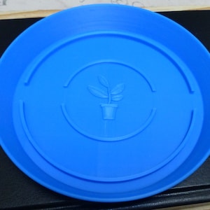 May include: A bright blue plastic plant saucer with a raised rim and a small plant icon in the centre.