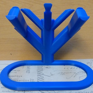 Op de afbeelding: Een blauwe plastic standaard met vijf takken, in de vorm van een boom, met een ronde basis. De standaard is ontworpen om meerdere items te houden, zoals tandenborstels of pennen.