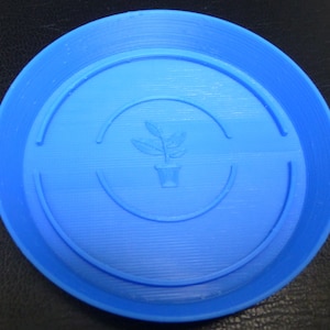 Puede incluir: Un platillo para plantas de plástico azul con un borde elevado y un icono de planta en el centro.