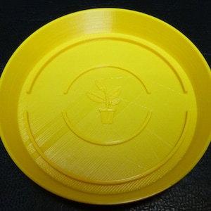 May include: A bright yellow plastic plant saucer with a raised rim and a small plant design in the centre.