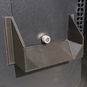 May include: A close-up of a black metal panel with a silver knob and a black plastic bracket. The bracket has a rectangular shape with a slight curve at the bottom.