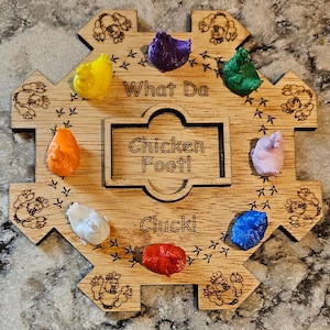 May include: A wooden game board with the words "What Da Chicken Foot!" and "Cluck!" printed on it. There are eight colorful chicken figurines placed around the board.