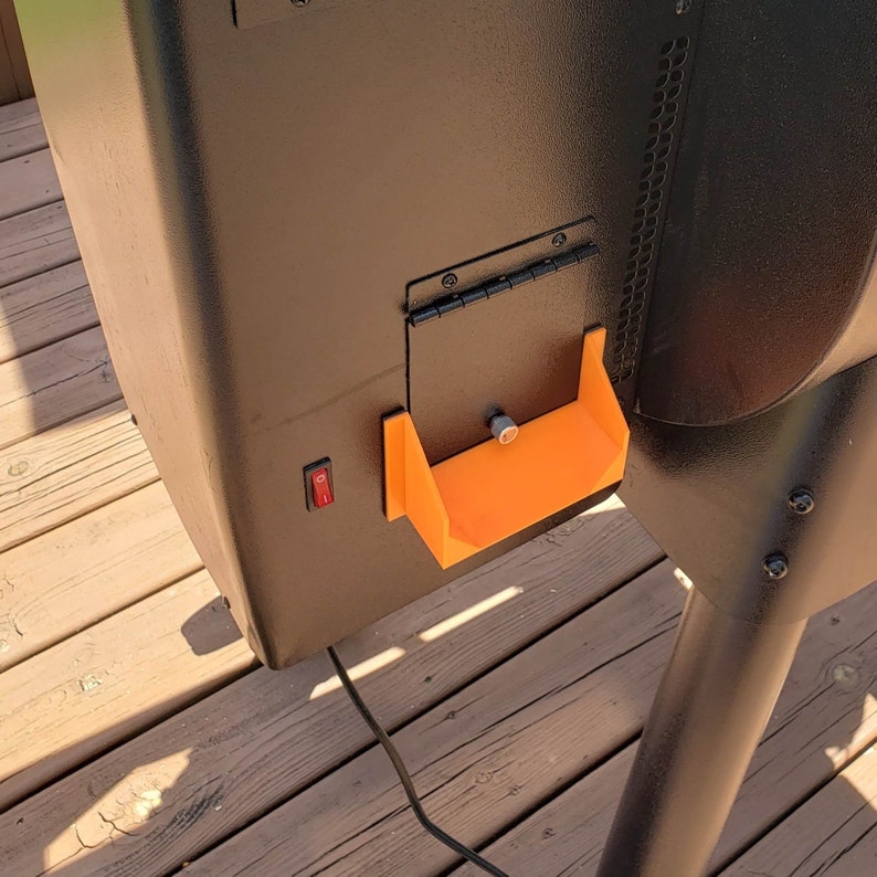 May include: A black metal smoker with an orange plastic ash pan and a black switch on the side.