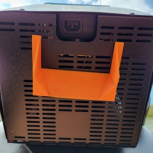 May include: Black metal box with a black power cord and an orange plastic handle. The box has a black metal grill on the back.