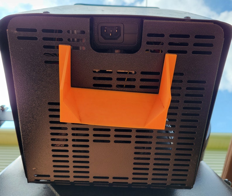 May include: Black metal box with a black power cord and an orange plastic handle. The box has a black metal grill on the back.