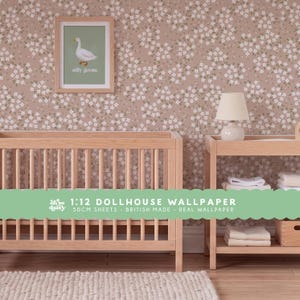 May include: Dollhouse wallpaper featuring a repeating pattern of small white flowers with green leaves on a dusty pink background. The wallpaper is displayed on a wall behind a wooden crib and a changing table. Text on the image reads 1:12 DOLLHOUSE WALLPAPER 50CM SHEETS - BRITISH MADE - REAL WALLPAPER.