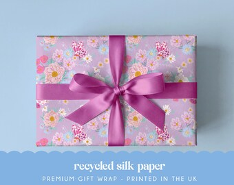 May include: A rectangular gift box wrapped in light purple paper featuring a repeating pattern of pink and white flowers and butterflies. A wide, smooth, dark pink satin ribbon is tied in a bow around the center of the box.