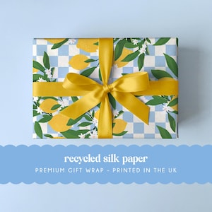 Może przedstawiać: Prezent owinięty żółtą wstążką. Papier do pakowania ma wzór cytryn, białych kwiatów i zielonych liści na niebiesko-białym kratkowanym tle. Widoczny jest napis "recycled silk paper".