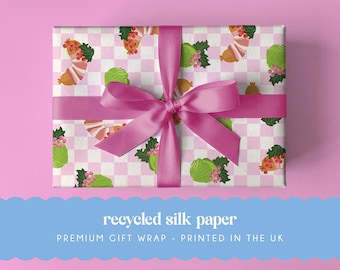 May include: A rectangular gift box wrapped in white and light pink checkered paper featuring a repeating pattern of green cabbages and brown sausages with red berries. A wide, vibrant pink satin ribbon is tied in a bow around the center.