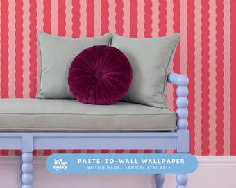 May include: A light blue bench with a grey seat cushion, a round dark purple velvet pillow, and two grey square pillows. The background features wallpaper with vertical wavy stripes in alternating shades of pink and red with text.