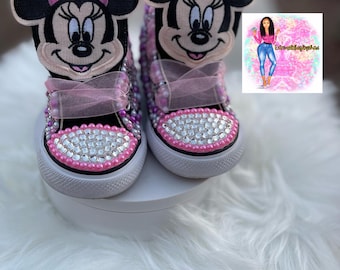 May include: A pair of black and pink high-top sneakers with a Minnie Mouse design. The sneakers are covered in rhinestones and have pink laces.