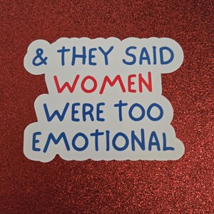 May include: A white sticker with a blue border and text that reads "& THEY SAID WOMEN WERE TOO EMOTIONAL." The word "WOMEN" is in red. The sticker is on a red glittery background.
