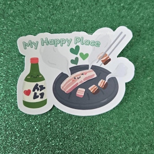 May include: A die-cut sticker featuring a green bottle with a red heart and Korean text, a black circular grill with pieces of pork belly, and the text My Happy Place. The pork belly pieces have faces, and there are green hearts and steam rising.