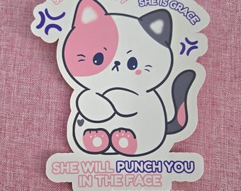 May include: A die-cut sticker featuring a white cat with a pink patch on its head and a dark gray tail. The cat has crossed arms and an angry expression. Text reads: SHE IS BEAUTY SHE IS GRACE SHE WILL PUNCH YOU IN THE FACE. Purple anger symbols.