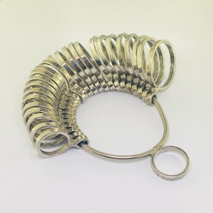 May include: A silver ring sizer with a series of graduated rings attached to a metal loop. The rings are arranged in a fan shape.