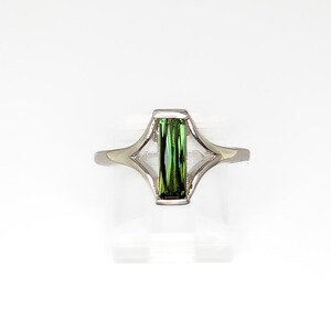 May include: A silver ring featuring a rectangular, vibrant green gemstone. The ring's design includes a geometric, openwork setting that cradles the gemstone. The band is a simple, polished silver.
