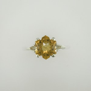 May include: A silver ring with a large, faceted, star-shaped, golden-brown gemstone.