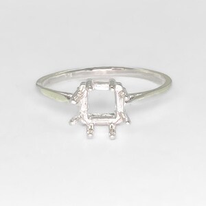 May include: Silver ring setting with a square shaped center for a gemstone.