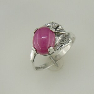 May include: A silver ring with a pink oval gemstone set in a leaf-shaped design.
