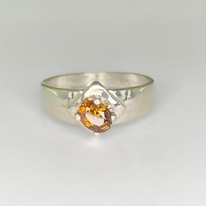 May include: A silver ring with a textured band and a round, orange gemstone set in a silver setting.