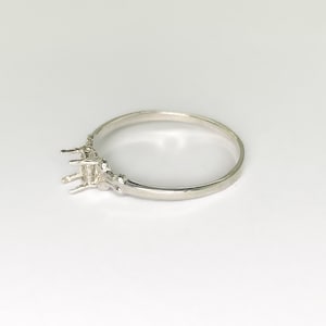 May include: A silver ring with a three-prong setting for a gemstone. The ring's band is smooth and polished, and the setting is detailed with small decorative elements. The ring is displayed on a white background.