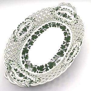 Może przedstawiać: Owalny biały ceramiczny półmisek z ażurowym wzorem na krawędziach. Naczynie posiada zielony wzór liści winogron i winorośli wokół wewnętrznego owalu i na uchwytach.