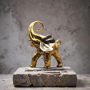 Peut inclure: Une figurine d'éléphant dorée, la trompe levée, posée sur un socle en pierre texturée. L'éléphant présente des détails fins et une finition polie. Il s'agit d'un objet décoratif, idéal pour la décoration intérieure.