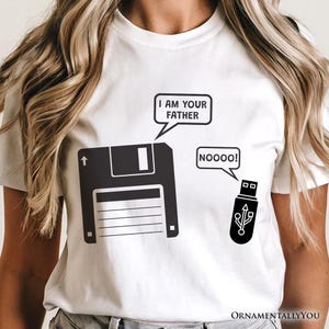 Könnte beinhalten: Ein weißes T-Shirt mit einer schwarzen Grafik einer Diskette und eines USB-Sticks. Die Diskette hat eine Sprechblase mit der Aufschrift I AM YOUR FATHER, und der USB-Stick hat eine Sprechblase mit der Aufschrift NOOOOO! Das Motiv ist mittig.