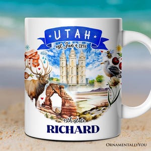 May include: White ceramic mug with a colorful illustration of Utah landmarks, including the Salt Lake Temple, Delicate Arch, and a red-rock landscape. The text "UTAH est. Jan 4, 1896 45th state RICHARD" is printed on the mug.
