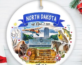 May include: A white ceramic ornament featuring a North Dakota theme. It includes a blue banner with "NORTH DAKOTA" and "est. Nov 2, 1889". The design showcases a plane, bison, horse, fish, and the state capitol building. The words "39th state" are also present.
